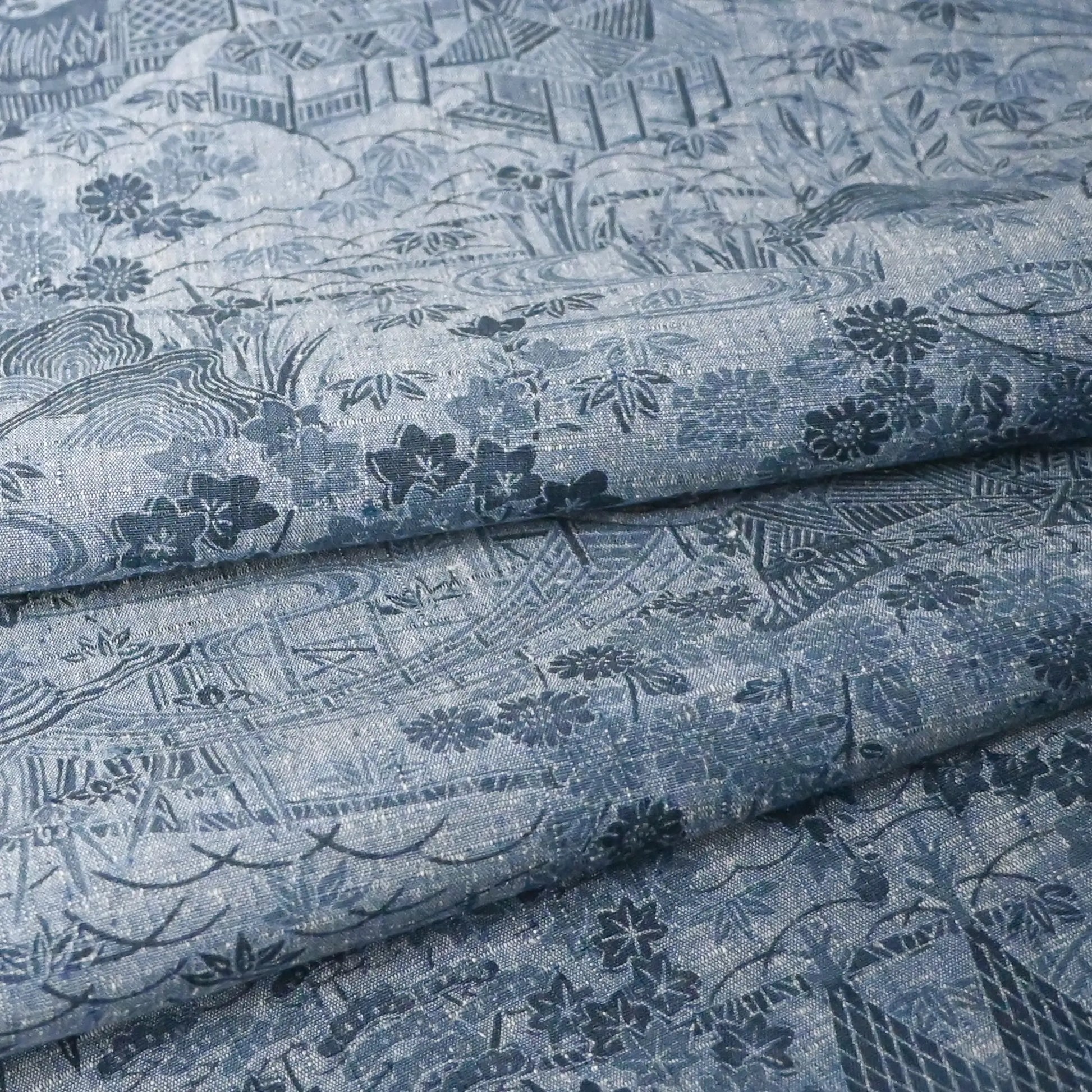 Detailed view of vintage women's tsumugi silk kimono fabric in steel blue with village scenery pattern.